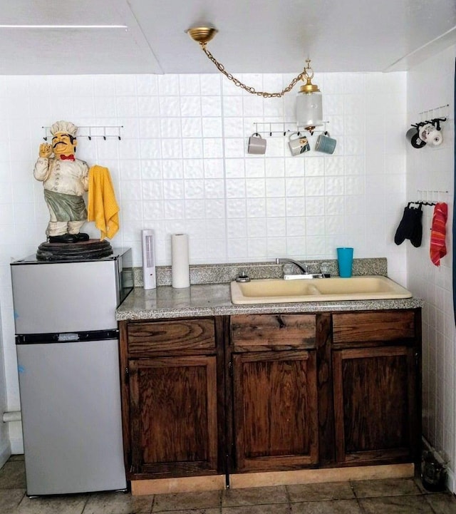 kitchen featuring tile walls, light countertops, dark brown cabinetry, a sink, and freestanding refrigerator