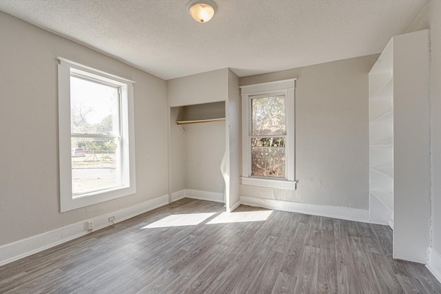 unfurnished bedroom with a textured ceiling, dark hardwood / wood-style floors, a closet, and multiple windows