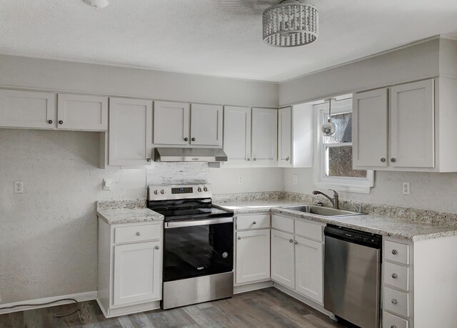 kitchen featuring light stone countertops, wood-type flooring, stainless steel appliances, sink, and white cabinets