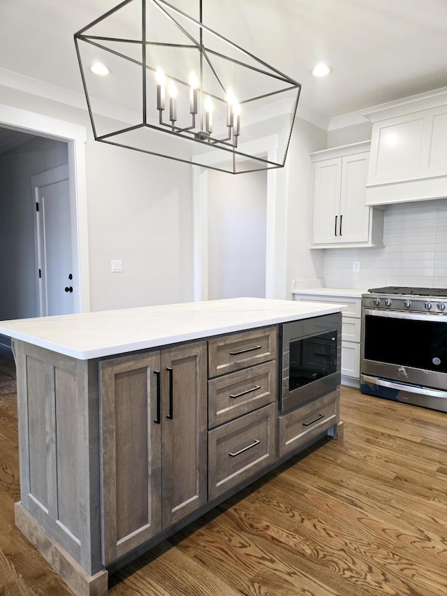 kitchen featuring white cabinets, decorative backsplash, ornamental molding, built in microwave, and stainless steel range