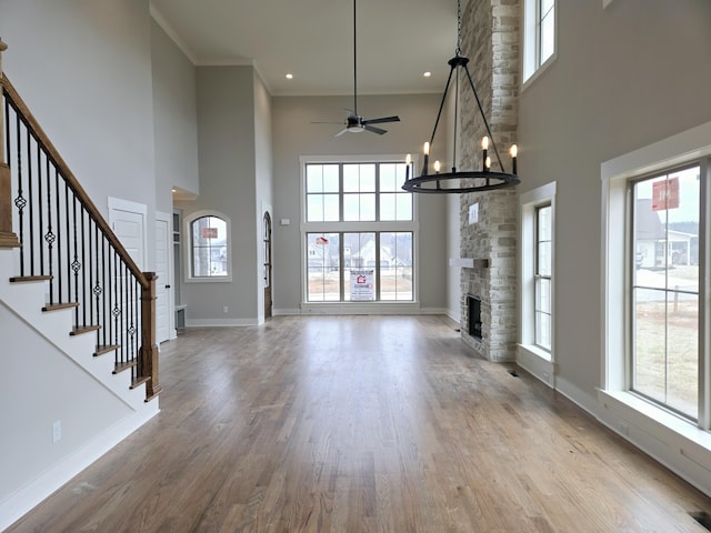 unfurnished living room featuring light wood-type flooring, a towering ceiling, a stone fireplace, and a wealth of natural light