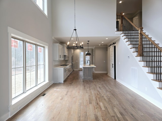 kitchen with light wood-type flooring, sink, pendant lighting, a barn door, and an island with sink