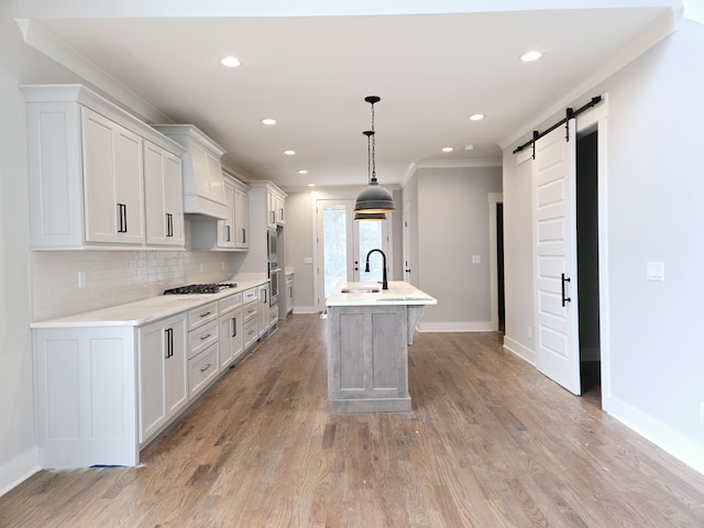 kitchen featuring white cabinetry, sink, a barn door, pendant lighting, and a kitchen island with sink