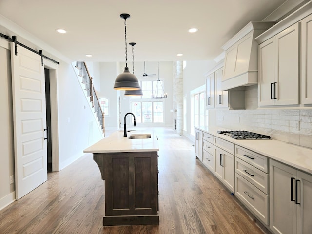 kitchen featuring a barn door, a kitchen island with sink, dark wood-type flooring, and sink