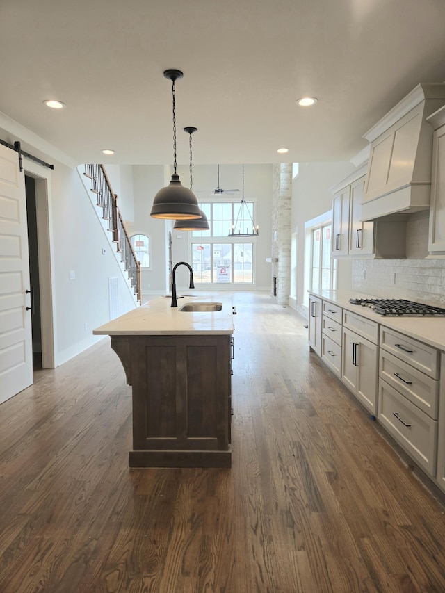 kitchen with sink, dark wood-type flooring, stainless steel gas cooktop, a barn door, and a center island with sink