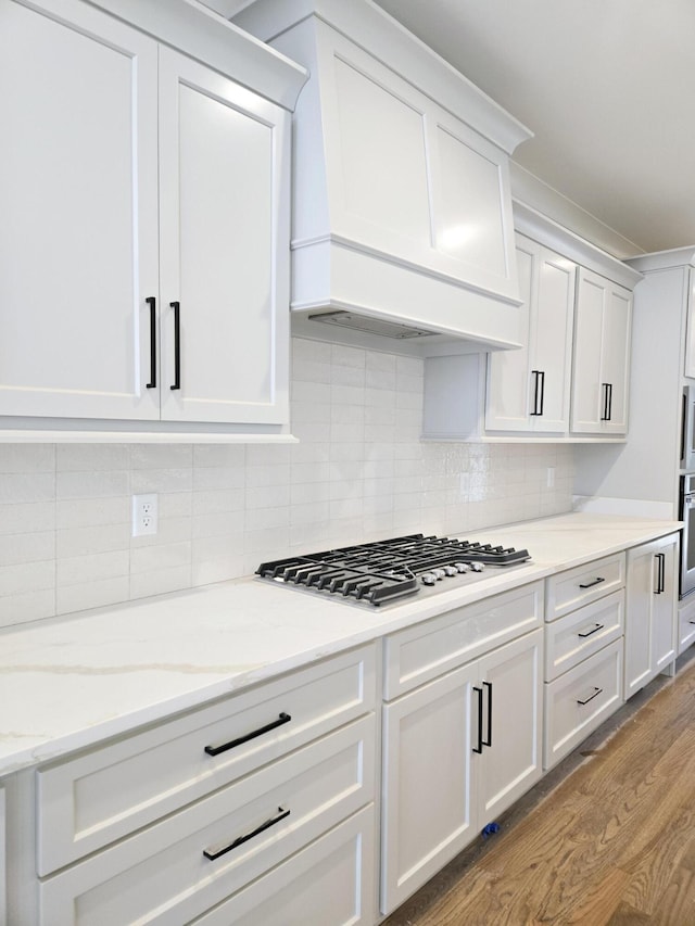 kitchen with white cabinetry, light stone countertops, stainless steel appliances, tasteful backsplash, and light wood-type flooring