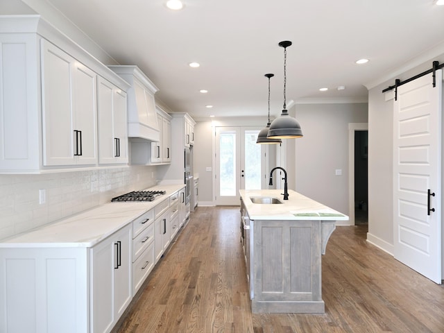 kitchen with sink, hanging light fixtures, an island with sink, wood-type flooring, and white cabinets