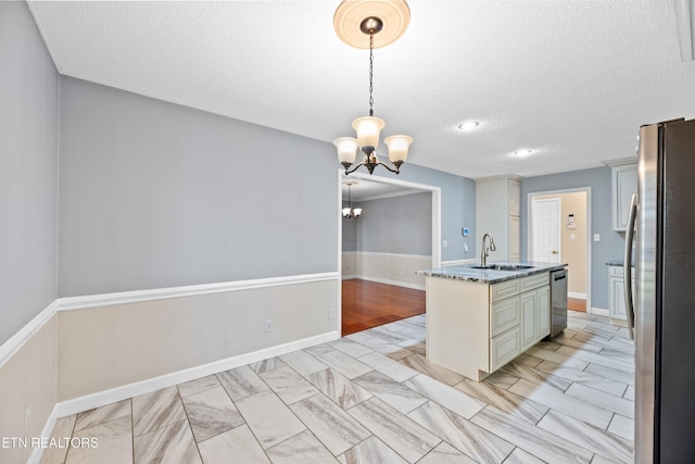 kitchen with a center island with sink, sink, hanging light fixtures, light stone counters, and stainless steel appliances