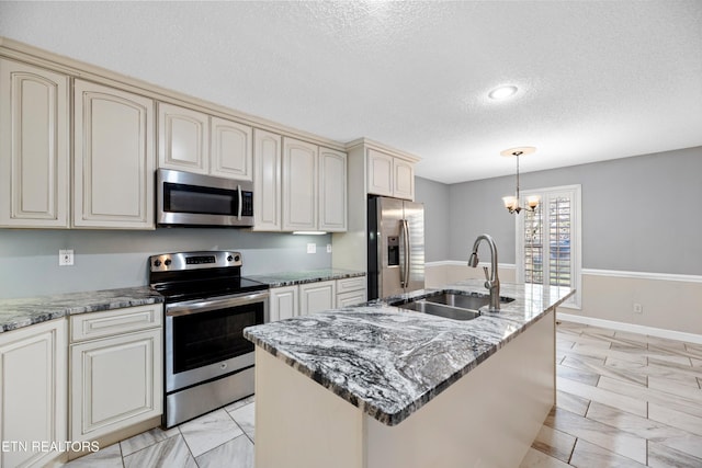 kitchen featuring pendant lighting, cream cabinets, a center island with sink, sink, and stainless steel appliances