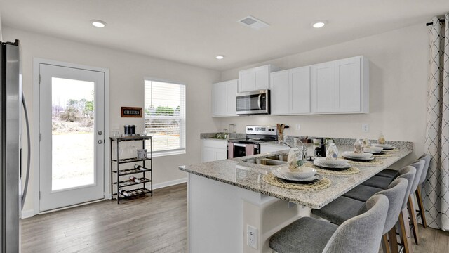 kitchen featuring light stone counters, stainless steel appliances, a kitchen bar, and white cabinets