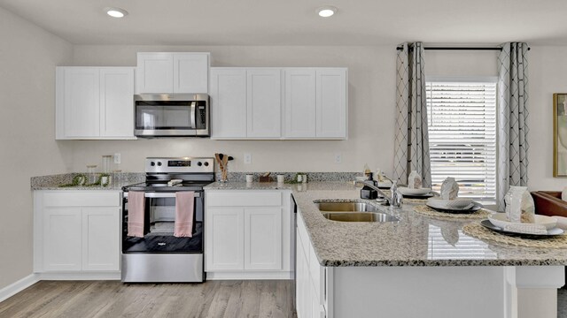 kitchen featuring appliances with stainless steel finishes, light stone countertops, light wood-type flooring, and white cabinets