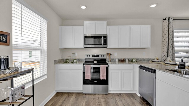 kitchen featuring white cabinetry, light stone counters, stainless steel appliances, and light hardwood / wood-style floors