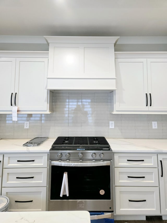 kitchen featuring light stone counters, white cabinets, stainless steel gas range, and tasteful backsplash