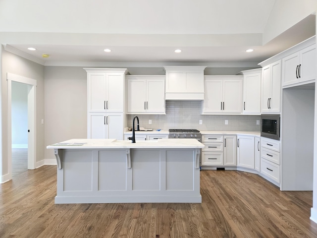 kitchen featuring white cabinets, built in microwave, stainless steel range with gas stovetop, and a center island with sink