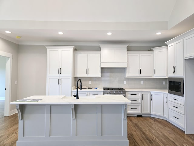 kitchen with white cabinets, high end stove, built in microwave, and an island with sink