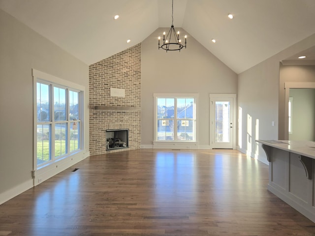 unfurnished living room with high vaulted ceiling, a brick fireplace, plenty of natural light, and a notable chandelier