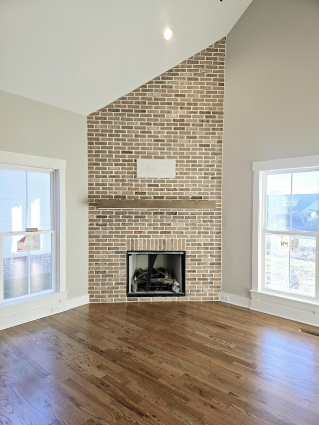 unfurnished living room featuring a brick fireplace, lofted ceiling, and wood-type flooring