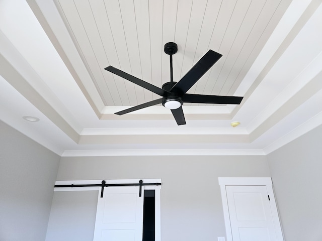 interior details featuring ceiling fan, crown molding, a barn door, and a tray ceiling