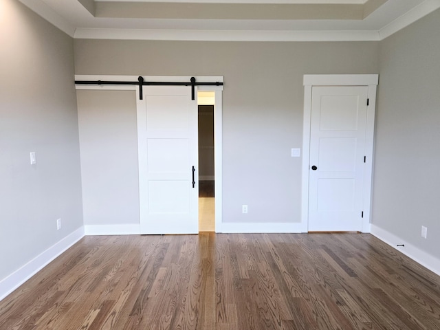 unfurnished bedroom featuring hardwood / wood-style floors, a closet, ornamental molding, and a barn door