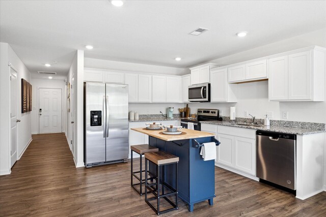 kitchen with dark hardwood / wood-style floors, appliances with stainless steel finishes, a kitchen bar, a center island, and white cabinets