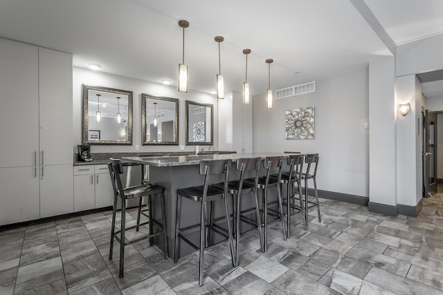 kitchen featuring dark stone countertops, white cabinetry, decorative light fixtures, and a breakfast bar