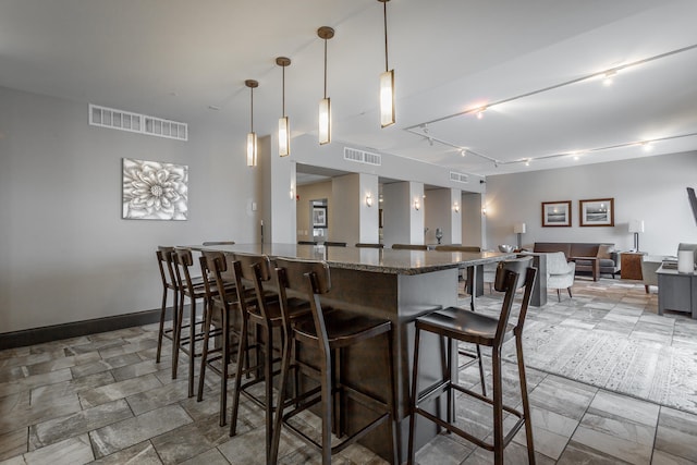 kitchen with a breakfast bar, hanging light fixtures, dark stone counters, and track lighting