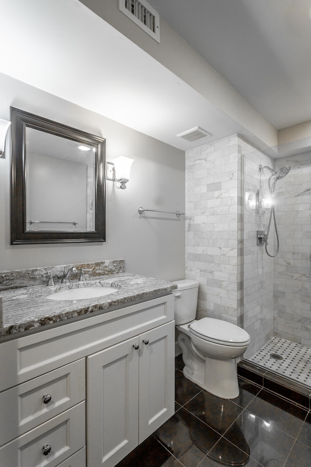 bathroom with tiled shower, vanity, toilet, and tile patterned flooring