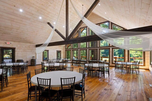 dining room with wood-type flooring, high vaulted ceiling, and wooden walls