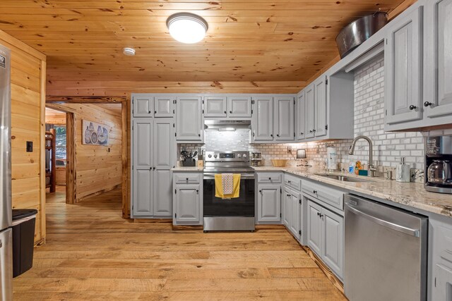 kitchen with wooden walls, appliances with stainless steel finishes, light stone countertops, light hardwood / wood-style floors, and sink