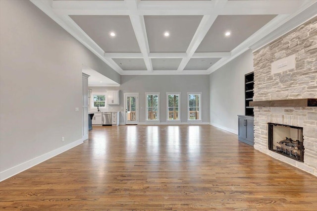 unfurnished living room featuring beamed ceiling, coffered ceiling, wood finished floors, a fireplace, and baseboards