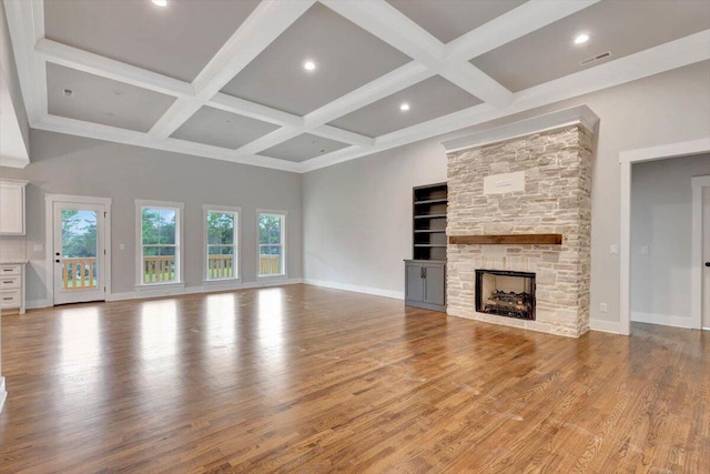 unfurnished living room with beamed ceiling, coffered ceiling, wood-type flooring, and a stone fireplace