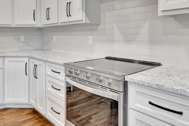 kitchen with light hardwood / wood-style flooring, high end stove, light stone countertops, and white cabinetry