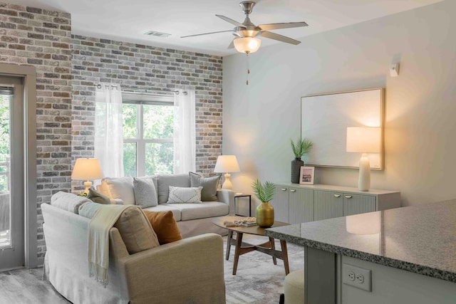 living room featuring brick wall, light hardwood / wood-style flooring, and ceiling fan