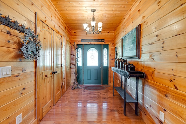 foyer entrance with wood ceiling, light wood-type flooring, wooden walls, and an inviting chandelier