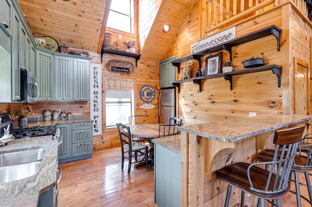 kitchen with a skylight, appliances with stainless steel finishes, kitchen peninsula, wood walls, and high vaulted ceiling