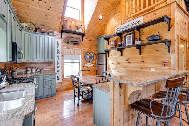 kitchen with high vaulted ceiling, wooden walls, a skylight, kitchen peninsula, and appliances with stainless steel finishes