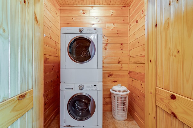 clothes washing area featuring stacked washer / dryer, light tile patterned floors, and wooden walls