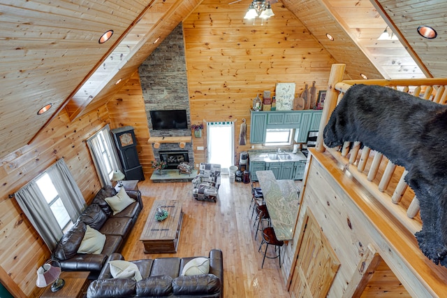 living room featuring a fireplace, high vaulted ceiling, wooden walls, wood-type flooring, and ceiling fan