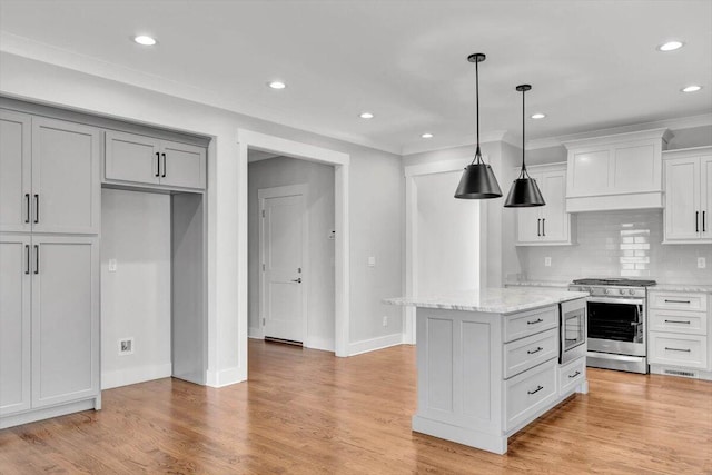 kitchen with appliances with stainless steel finishes, a kitchen island, light stone counters, and light hardwood / wood-style floors