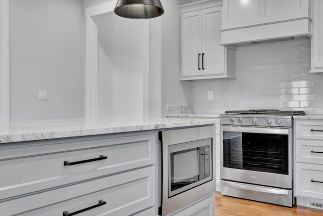 kitchen featuring light stone countertops, light hardwood / wood-style flooring, backsplash, appliances with stainless steel finishes, and custom exhaust hood