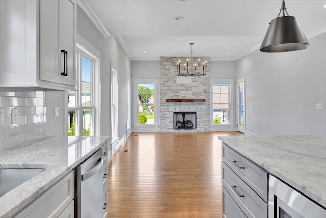 kitchen featuring an inviting chandelier, light wood-type flooring, light stone countertops, a stone fireplace, and stainless steel dishwasher