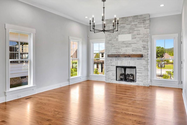 unfurnished living room with light wood-type flooring, a fireplace, a notable chandelier, and a healthy amount of sunlight