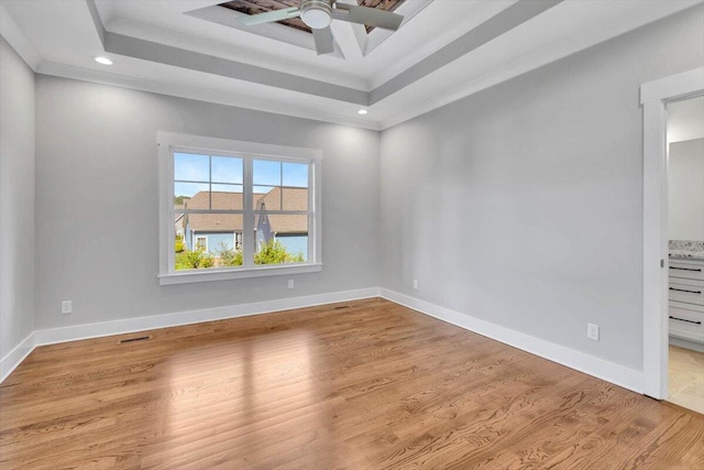 empty room featuring ceiling fan, light wood-type flooring, and a tray ceiling