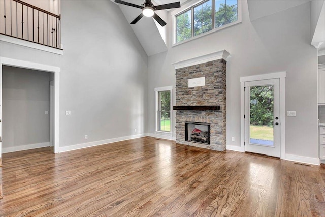 unfurnished living room with a stone fireplace, plenty of natural light, wood finished floors, and ceiling fan