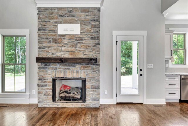 unfurnished living room with a stone fireplace, visible vents, baseboards, and wood finished floors