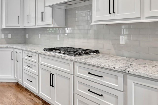 kitchen with white cabinets, light wood-type flooring, under cabinet range hood, and stainless steel gas cooktop