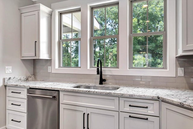 kitchen with decorative backsplash, white cabinets, dishwasher, and a sink