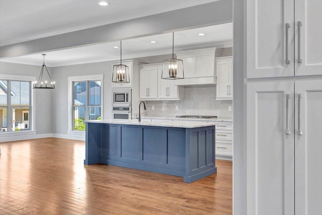 kitchen featuring light hardwood / wood-style flooring, an island with sink, hanging light fixtures, appliances with stainless steel finishes, and white cabinets