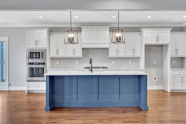 kitchen featuring a center island with sink, hardwood / wood-style floors, light stone countertops, and appliances with stainless steel finishes