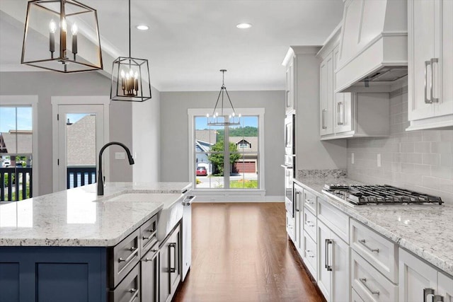 kitchen with an island with sink, hanging light fixtures, a notable chandelier, and premium range hood